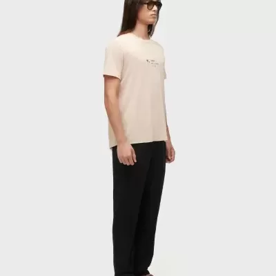 Homem com t-shirt bege, calças pretas e sandálias castanhas