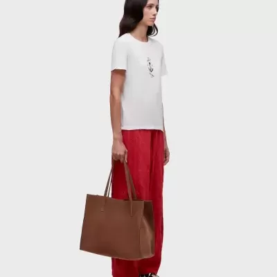 Mulher com camiseta branca com estampa e calças vermelhas segurando bolsa castanha e sapatos com padrão animal print