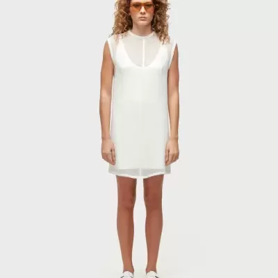 Mulher com vestido branco curto e sandálias brancas, usando óculos de sol laranja