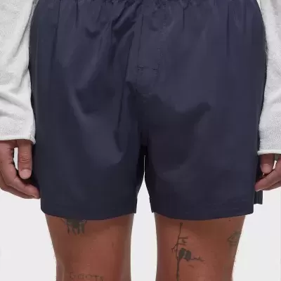 Cuecas tipo boxers azuis escuras com cintura elástica preta vestidas por homem com camisola branca e pernas tatuadas