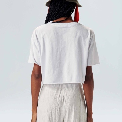 Pessoa de costas com chapéu verde, t-shirt branca e calças bege