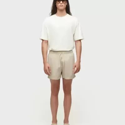 Homem com roupa casual bege e branca, óculos escuros, em fundo branco.