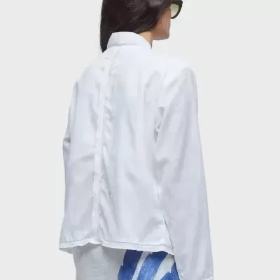 Pessoa de costas com camisa branca de manga comprida e saia azul e branca, fundo branco