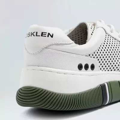Parte lateral e traseira de ténis branco com detalhes verdes e pontos pretos, com texto OSKLEN na pala