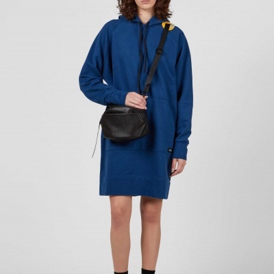 Mulher com vestido azul escuro e bolsa preta em fundo cinzento.