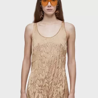 Blusa bege enrugada sem mangas com óculos de sol amarelos.