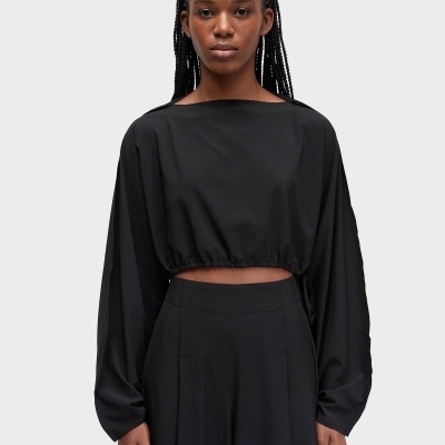 Top cropped preto com mangas largas e calças pretas, modelo em fundo cinzento.