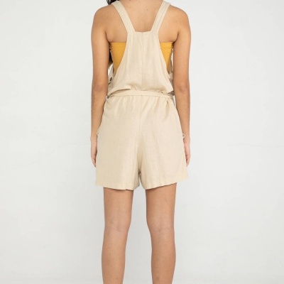 Mulher de costas vestindo macacão curto bege e top amarelo