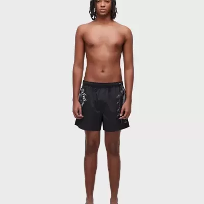 Homem com calções de banho pretos com padrão branco e chinelos castanhos