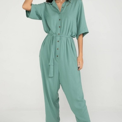 Mulher a usar macacão verde com botões castanhos e sapatos tipo chinelo bege