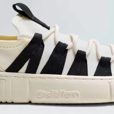 Tênis branco com tiras pretas e sola grossa branca com nome Osklen em relevo