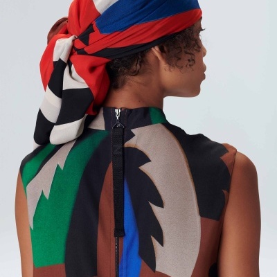 Pessoa com lenço colorido ao cabelo e vestido com padrão abstrato e fecho nas costas