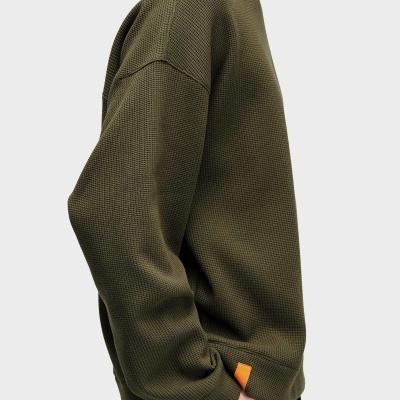Sweatshirt verde oliva de malha grossa com gola redonda e etiqueta laranja na parte inferior.