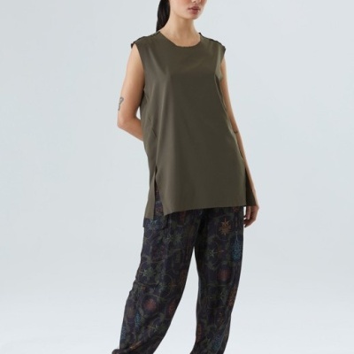 Mulher com camisola verde escura sem mangas e calças pretas com padrão colorido