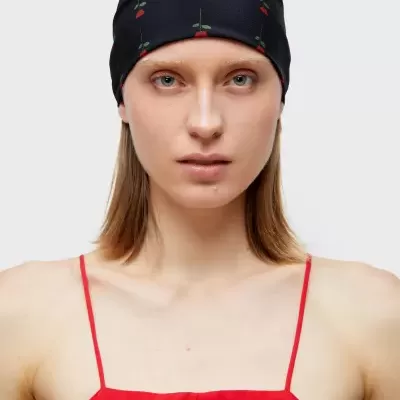 Pessoa com capa preta decorada com flores vermelhas e vestido vermelho em fundo branco.