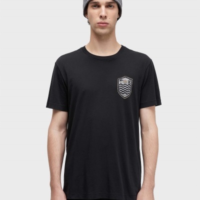 Pessoa com t-shirt preta com emblema prateado, gorro cinza e calças pretas