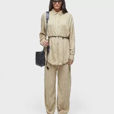 Conjunto feminino bege com camisa de manga comprida e calças largas, cinto preto, bolsa e sandálias pretas