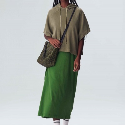 Mulher com camisola verde-oliva com capuz, saia verde, meias brancas e ténis, com bolsa verde de padrão entrelaçado