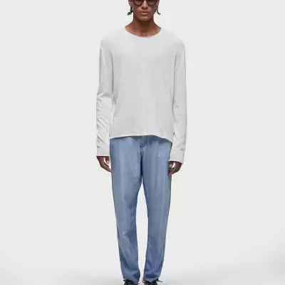 Homem com t-shirt branca de manga comprida e calças azuis claras, calçado com ténis pretos