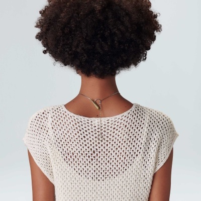 Pessoa de costas com blusa de malha branca e cabelo encaracolado.