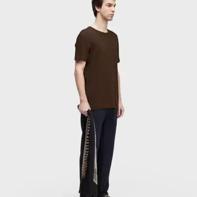 Homem vestindo t-shirt castanha, calças pretas e sandálias, segurando tecido com padrão de ossos.