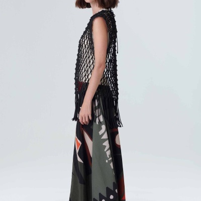 Mulher com vestido longo estampado e colete de malha preta em fundo cinza claro