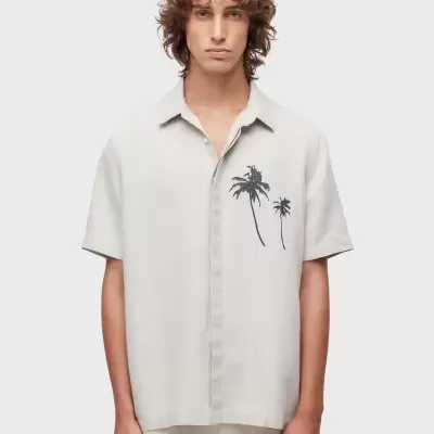 Camisa bege claro de manga curta com palmeiras pretas, gola clássica, usada por homem.