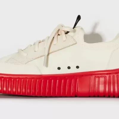 Sapatilha desportiva branca com sola vermelha e detalhes pretos