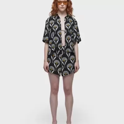 Conjunto feminino com padrão de folhas, camisa e calções pretos com detalhes amarelos e brancos.