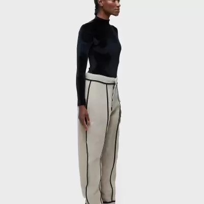 Modelo de pé com camisola preta de gola alta e calças largas bege com costuras pretas