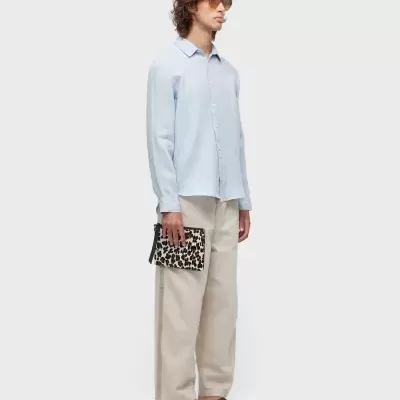 Homem com camisa azul clara, calças largas bege, sandálias castanhas e carteira leopard print