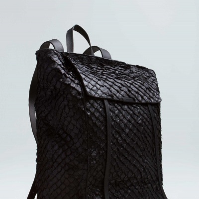 Mochila preta com textura de escamas sobre fundo cinzento claro