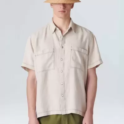 Homem com camisa bege de manga curta, calções verdes bordados e chapéu de palha