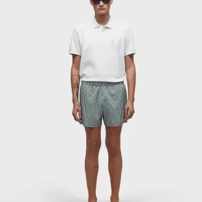 Homem com t-shirt polo branca, calções às riscas e chinelos pretos