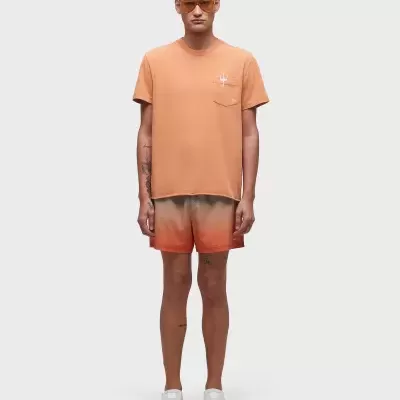 Homem com t-shirt laranja, calções degradados laranja e creme, e ténis brancos