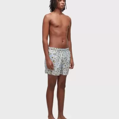 Homem com calções de banho florais e chinelos castanhos.