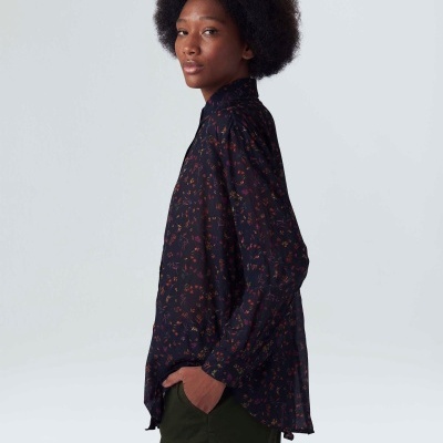 Camisa feminina preta com padrão floral vermelho e laranja, vista lateral, combinada com calças verde-escuro.