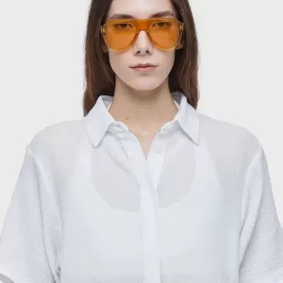 Mulher com óculos de sol âmbar com lentes laranja e camisa branca