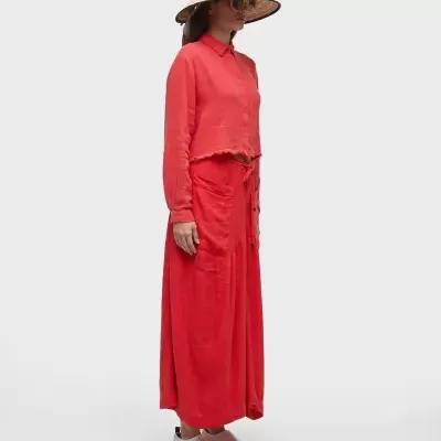 Mulher vestindo conjunto vermelho com camisa e saia, chapéu de palha estampado e sapatos brancos com detalhe vermelho