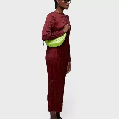 Mulher de vestido longo bordô com bolsa verde lima e sapatos pretos.