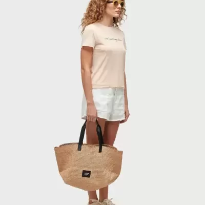 Mulher com t-shirt rosa, calções brancos e mala de palha com alças pretas e etiqueta