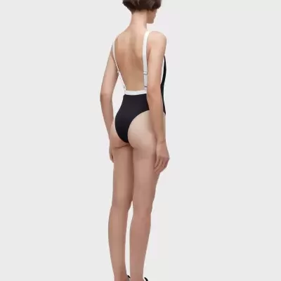 Mulher com fato de banho preto e alças brancas visto de costas com sapatilhas.