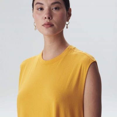 Blusa amarela sem mangas com gola redonda usada por mulher com brincos dourados