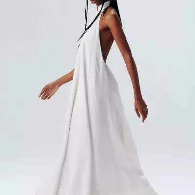 Mulher com vestido longo branco e sandálias pretas em fundo claro