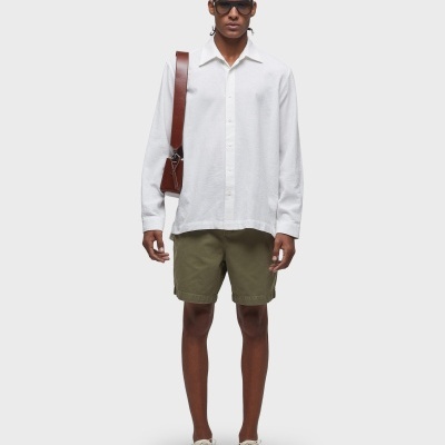 Homem com camisa branca, calções verde oliva, ténis brancos e mala castanha ao ombro