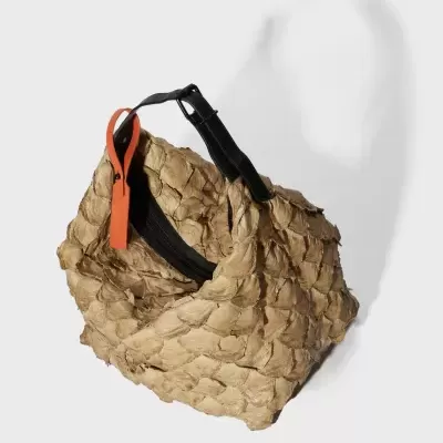 Mala bege com textura de escamas, alças pretas e pendente laranja