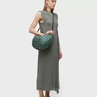 Mulher com vestido cinzento, bolsa verde texturizada e sapatos castanhos.