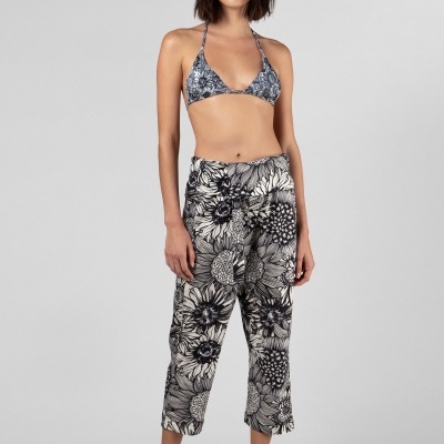 Modelo com biquíni cinza estampado, calças florais preto e branco, chapéu tipo pescador e sandálias.