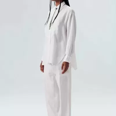 Pessoa vestindo camisa e calças brancas com sandálias castanhas, fundo branco