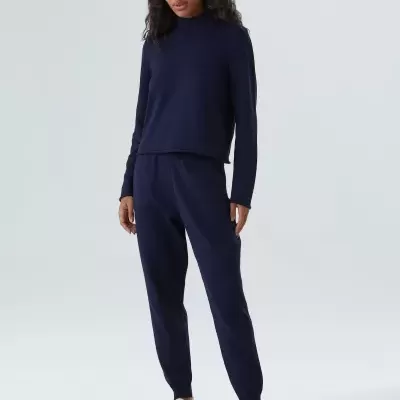 Mulher a vestir conjunto azul escuro com sapatilhas brancas em fundo cinzento liso